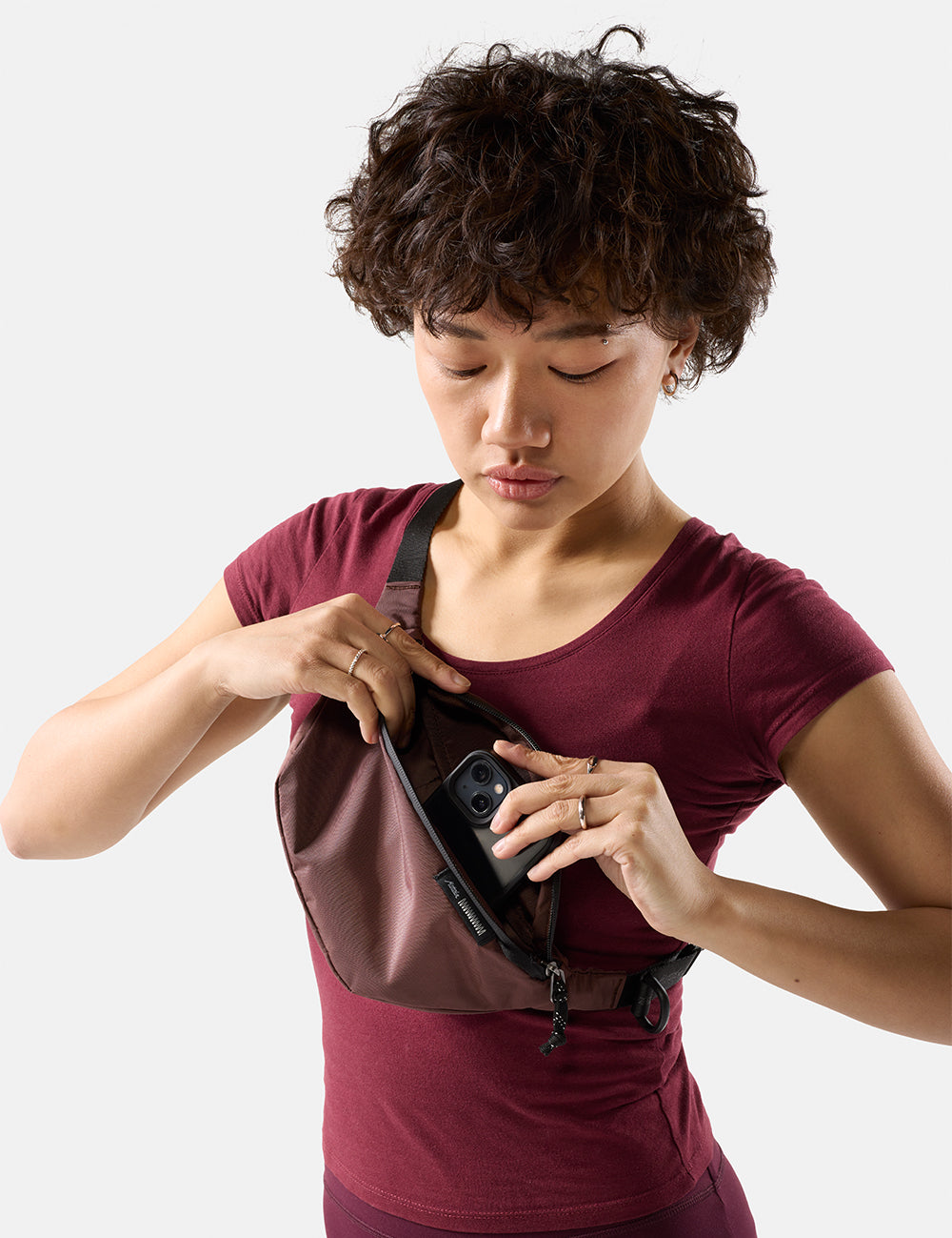 Woman in a maroon shirt holding a garnet sling with a phone inside on a white background