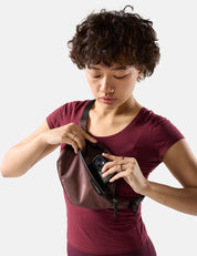Woman in a maroon shirt holding a garnet sling with a phone inside on a white background