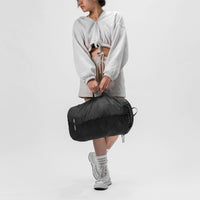 woman standing on white studio background, holding packed up laundry bag by its side carry handle