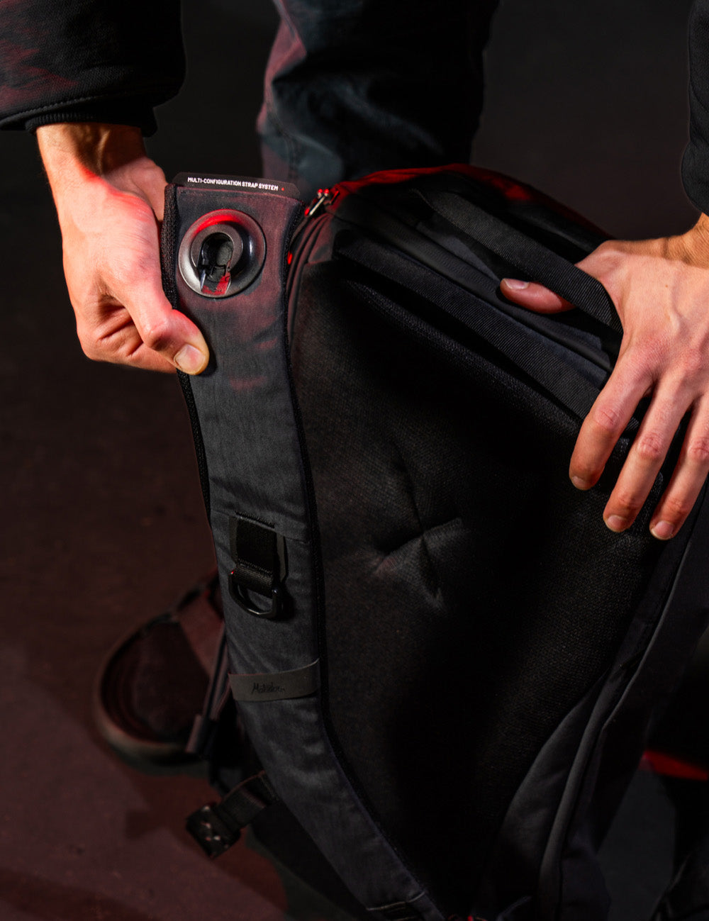Person holding a black bag with a red strap on a dark background