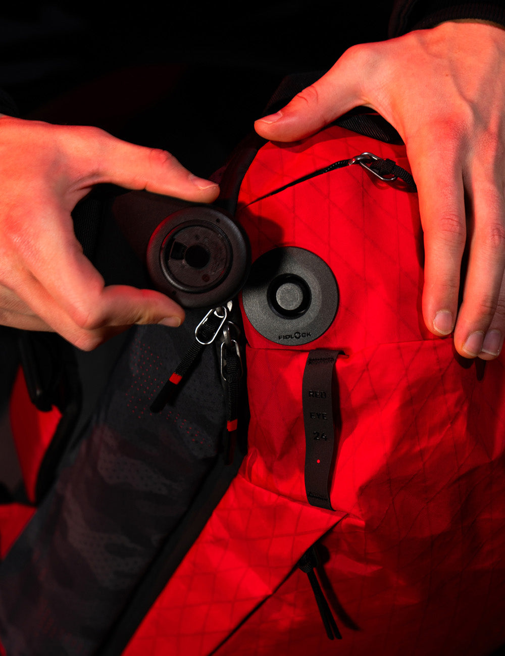 Close-up of hands adjusting a black strap on a red backpack with a visible brand logo.
