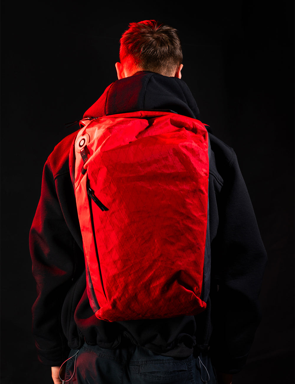 man wearing red backpack in black setting