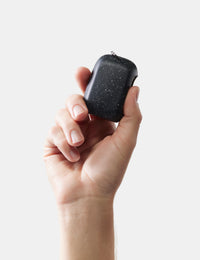 Hand holding a small black towel case with a textured surface on a light gray background