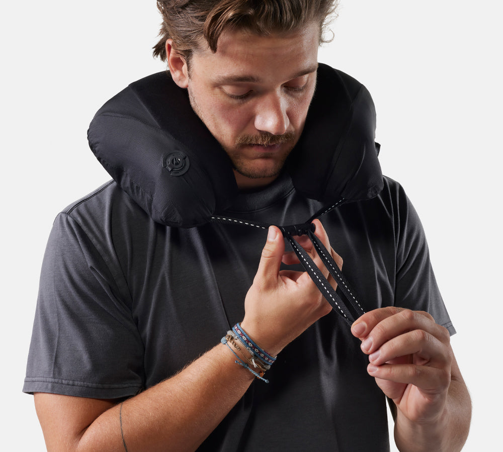 Man wearing a black neck pillow against a white background