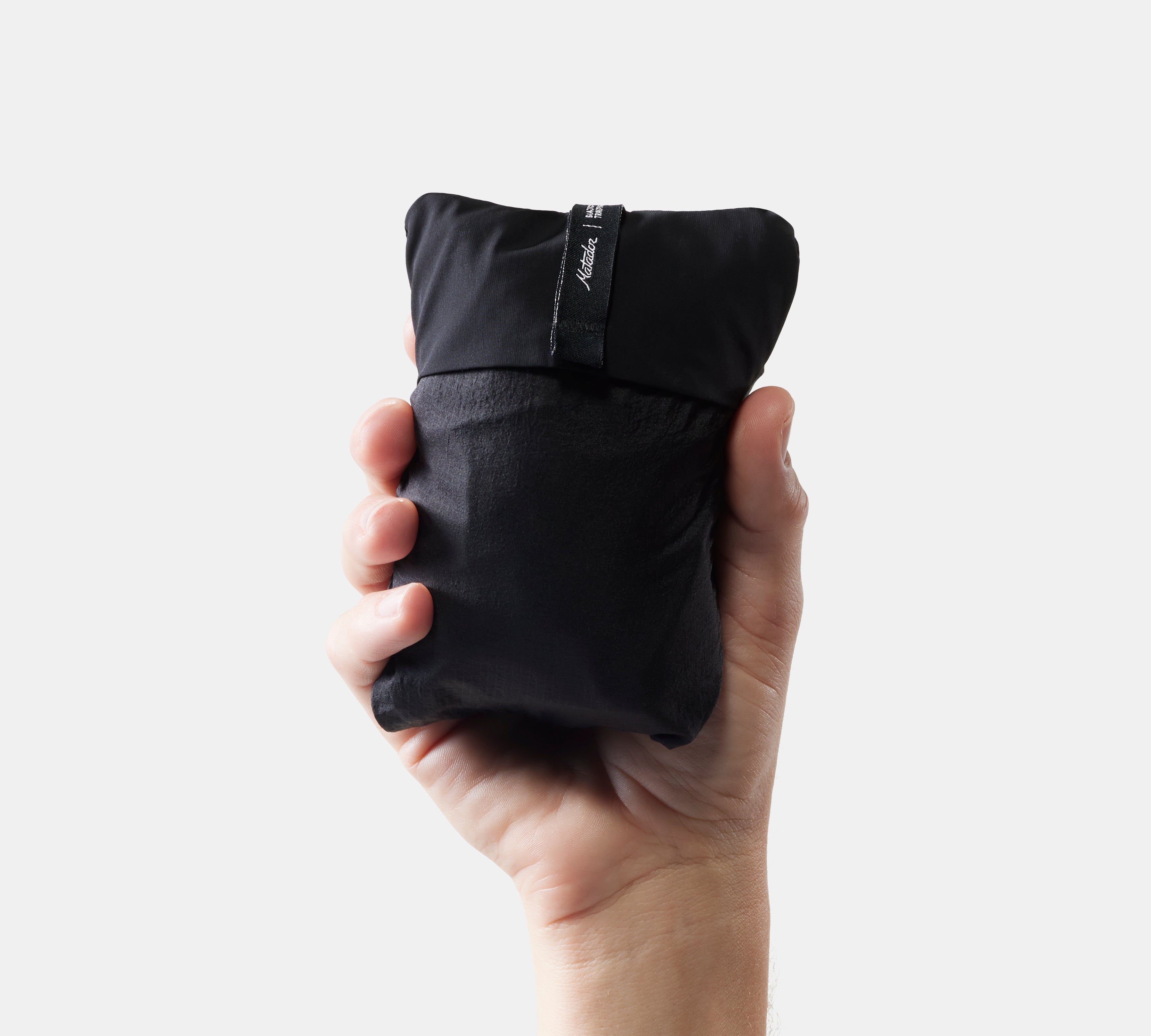 Hand holding a packed black travel pillow against a white background