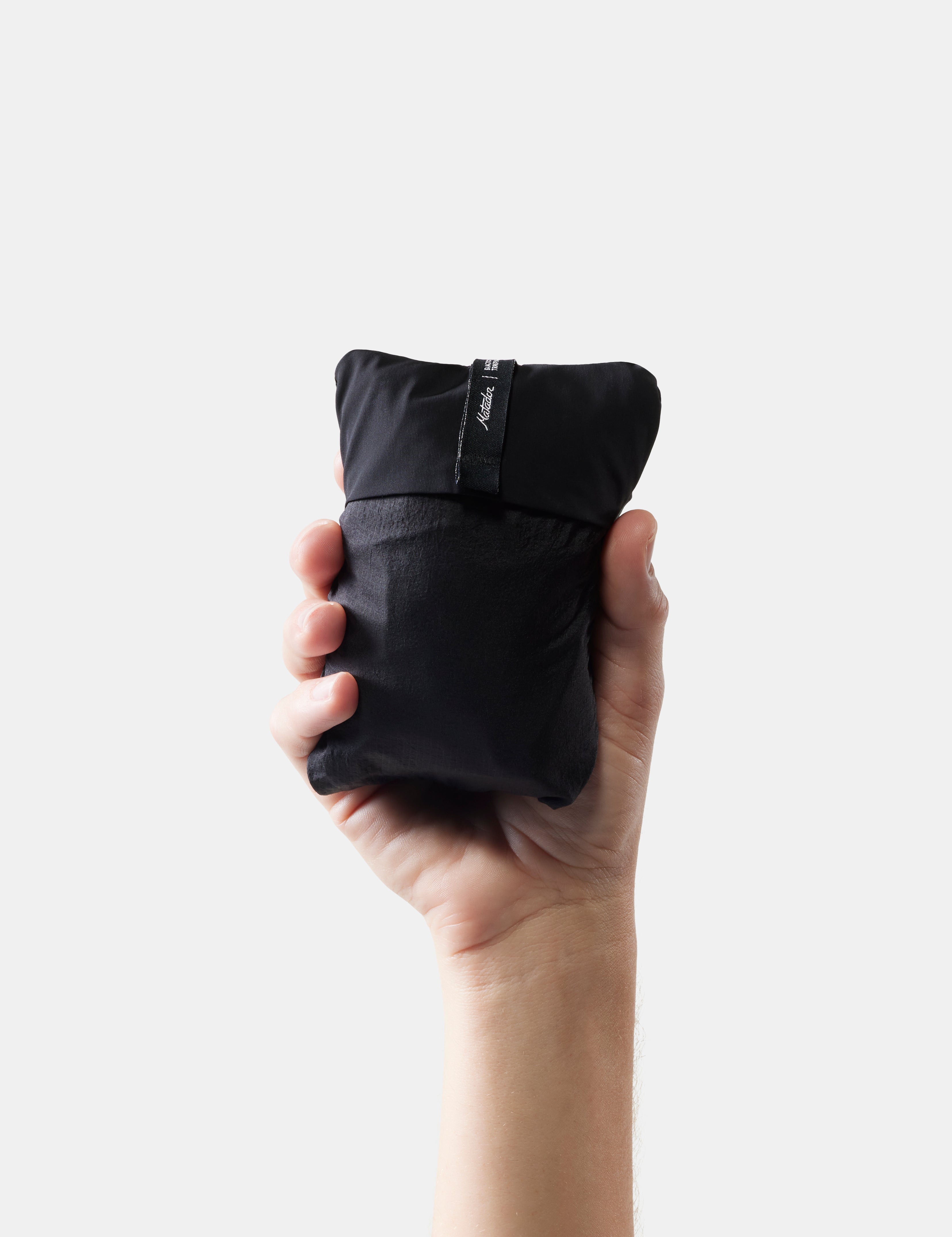 Hand holding a packed black travel pillow against a white background