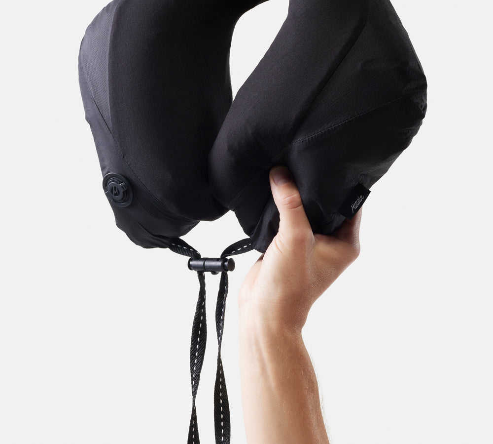 Black travel neck pillow held by a hand against a white background