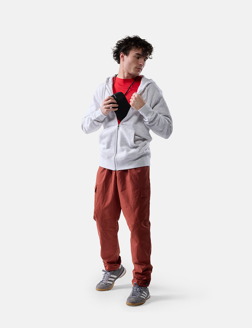 man on white background placing travel neck wallet inside his zip up sweatshirt
