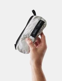 Hand holding a white pouch against a light gray background