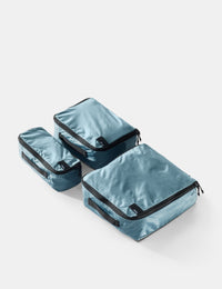 Set of three blue packing cubes with black zippers on a light gray background