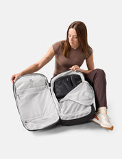Woman sitting on the floor with a large open backpack, showing its compartments with packing cubes