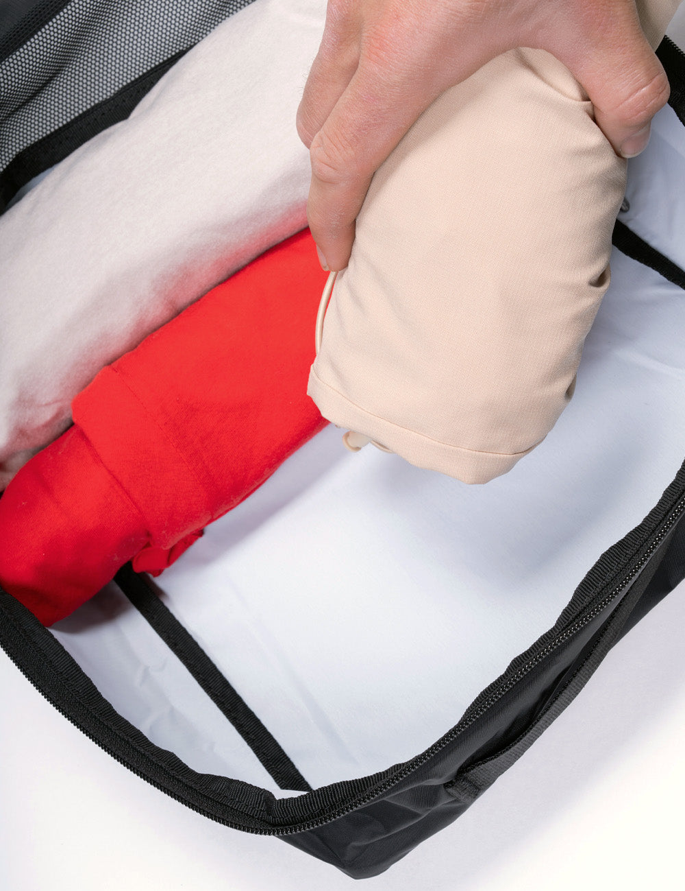 hand putting rolled clothing into black packing cube with white interior