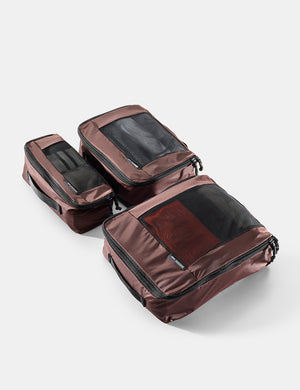 Set of three garnet travel packing cubes on a light gray background