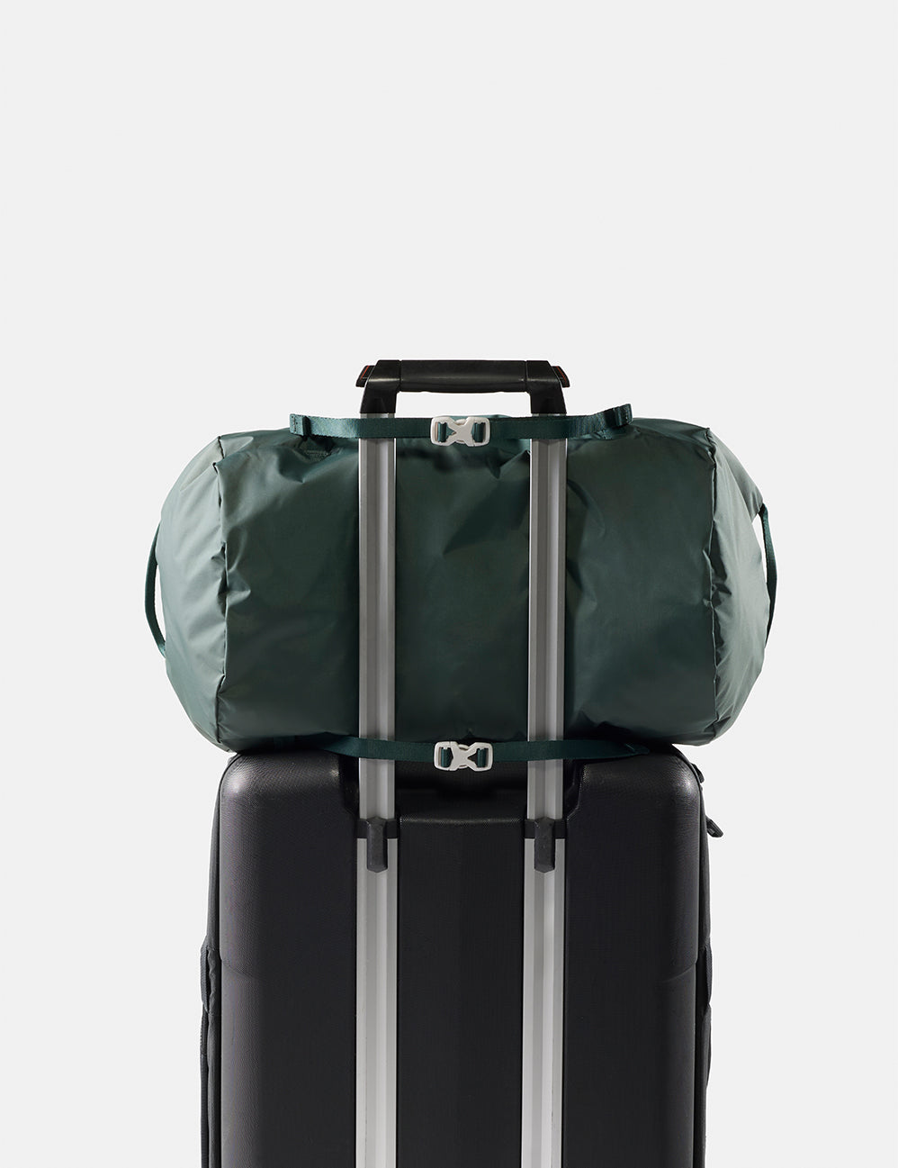 Green duffel bag tied to a black suitcase on a light gray background