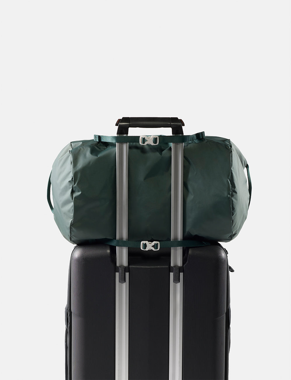 Green duffel bag tied to a black suitcase on a light gray background