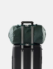 Green duffel bag tied to a black suitcase on a light gray background