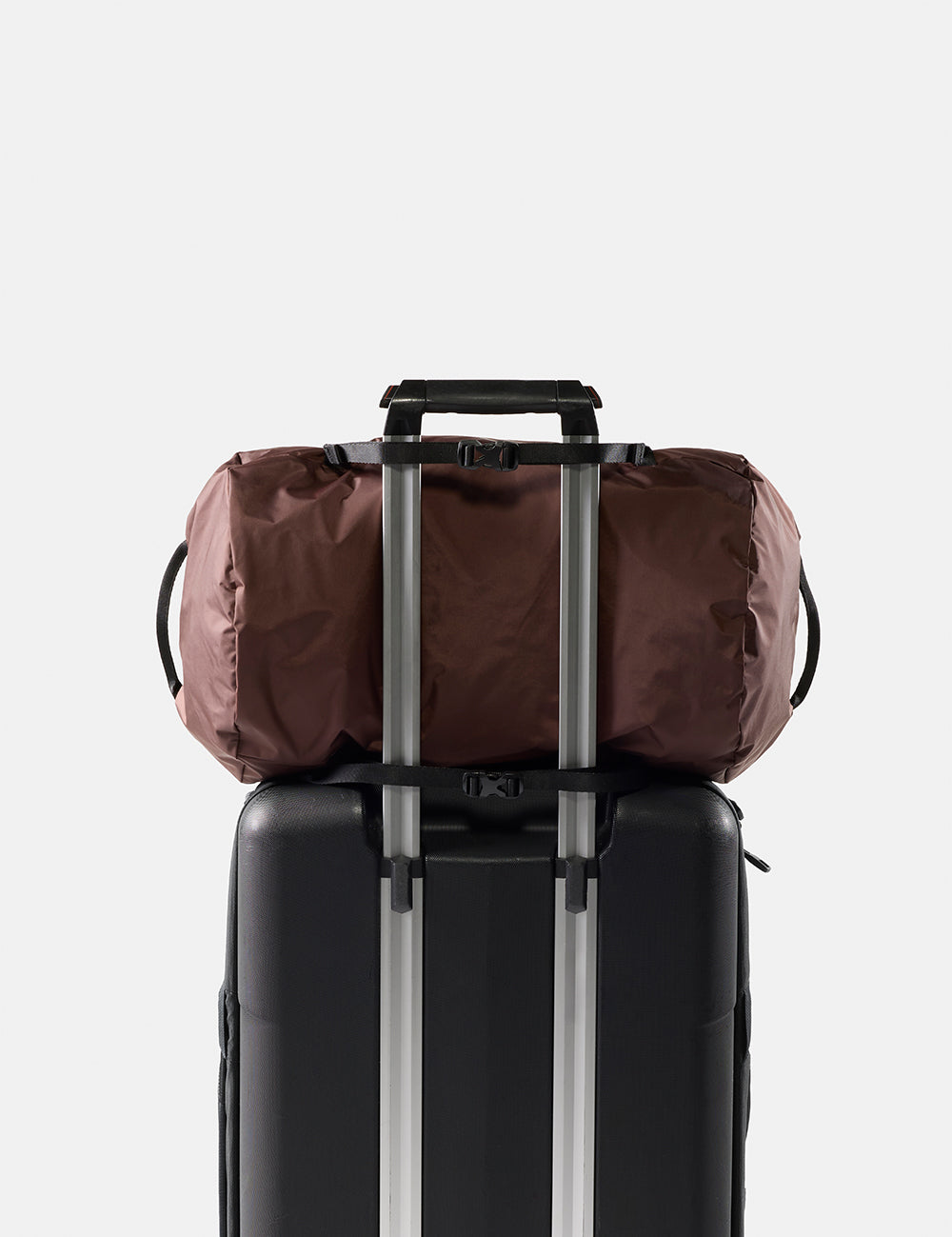 garnet duffel bag secured to a black suitcase with straps on a light gray background