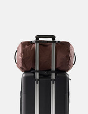 garnet duffel bag secured to a black suitcase with straps on a light gray background