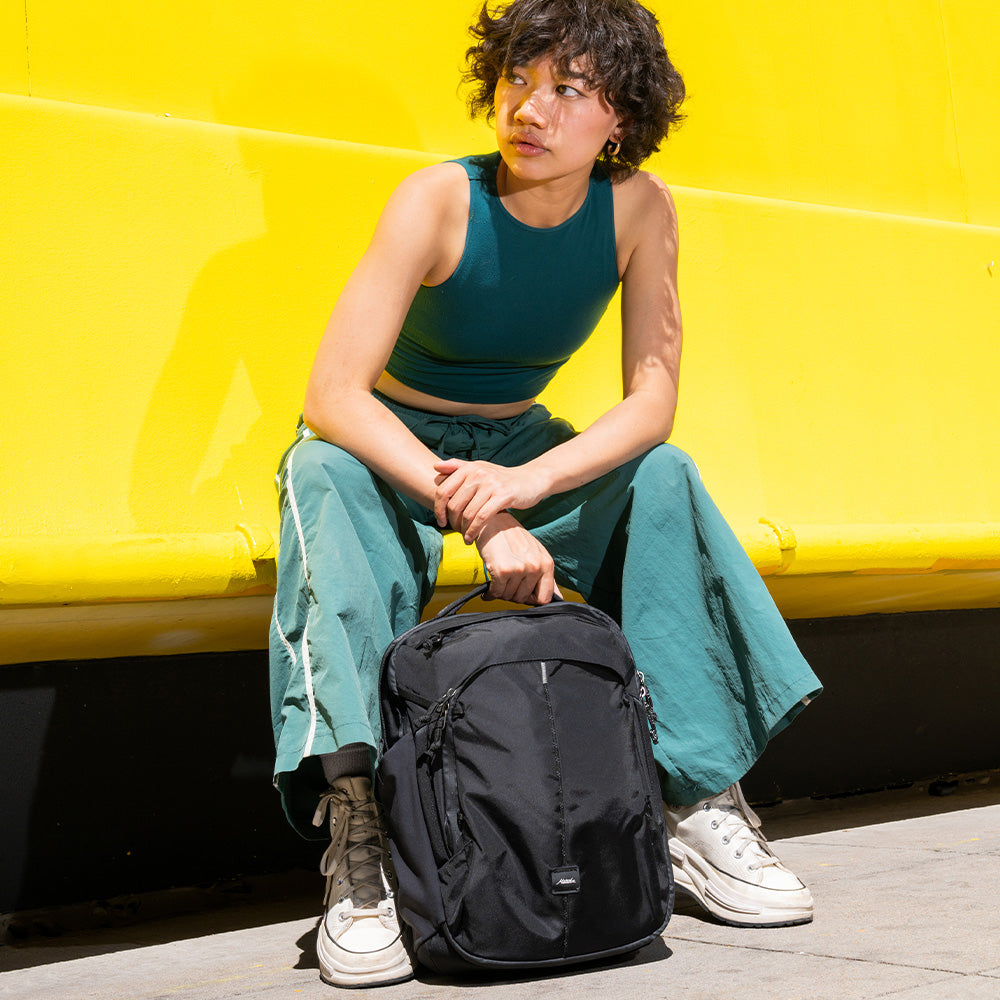 person in green in front of yellow wall with black backpack