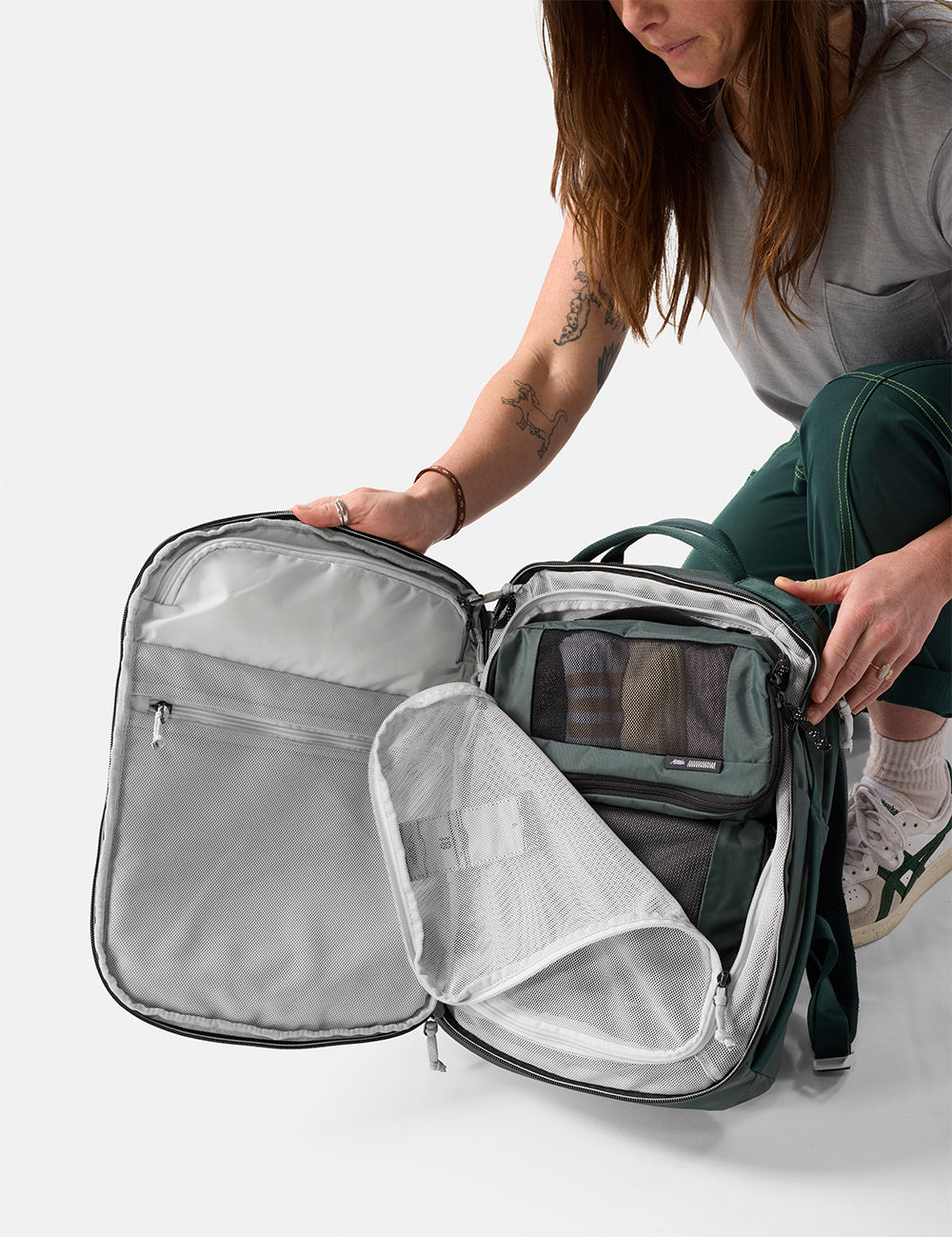 Person opening a green travel backpack with a clear front pocket on a white background