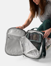 Person opening a green travel backpack with a clear front pocket on a white background