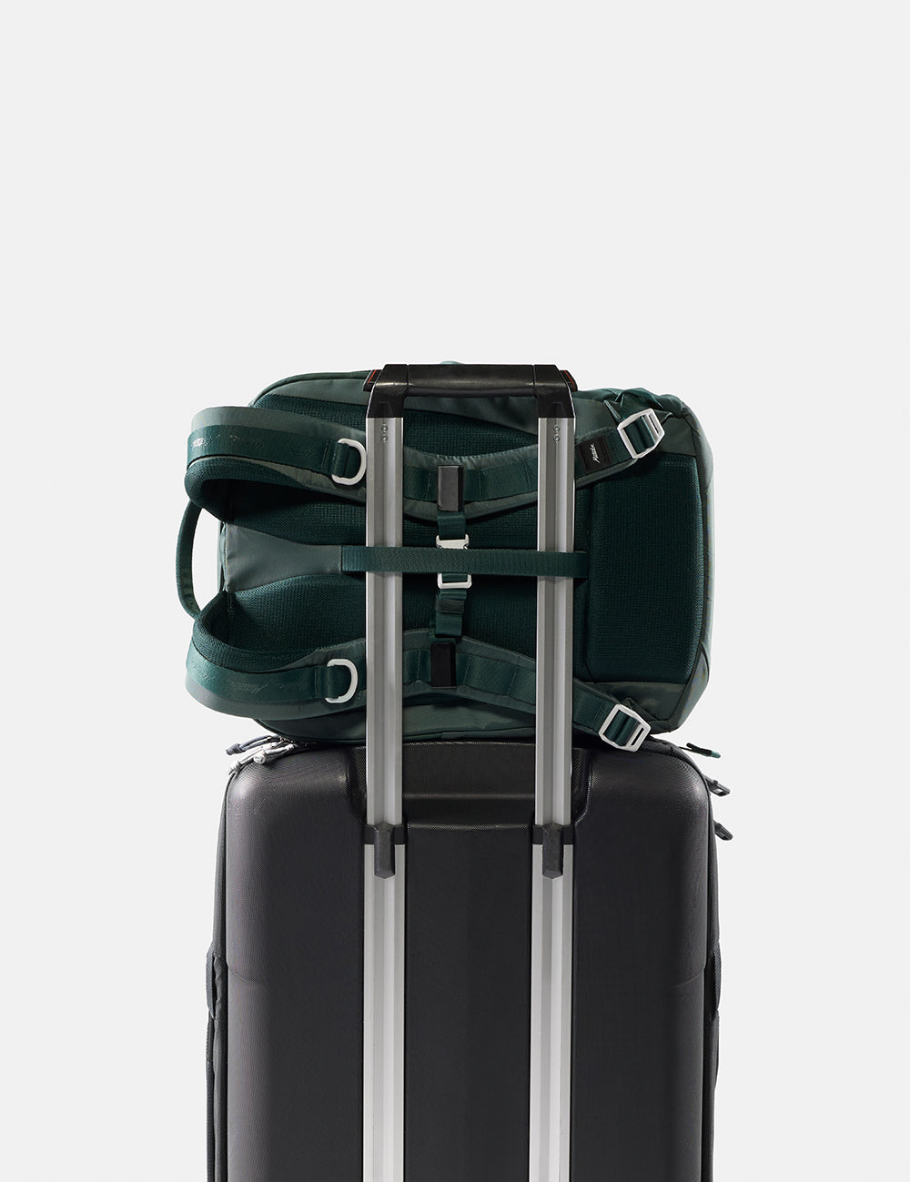Green backpack attached to a black suitcase on a light gray background