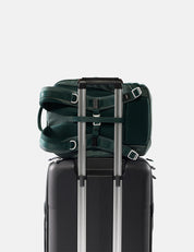Green backpack attached to a black suitcase on a light gray background
