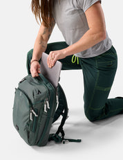 Person kneeling on a white surface with a green backpack and gray shirt.