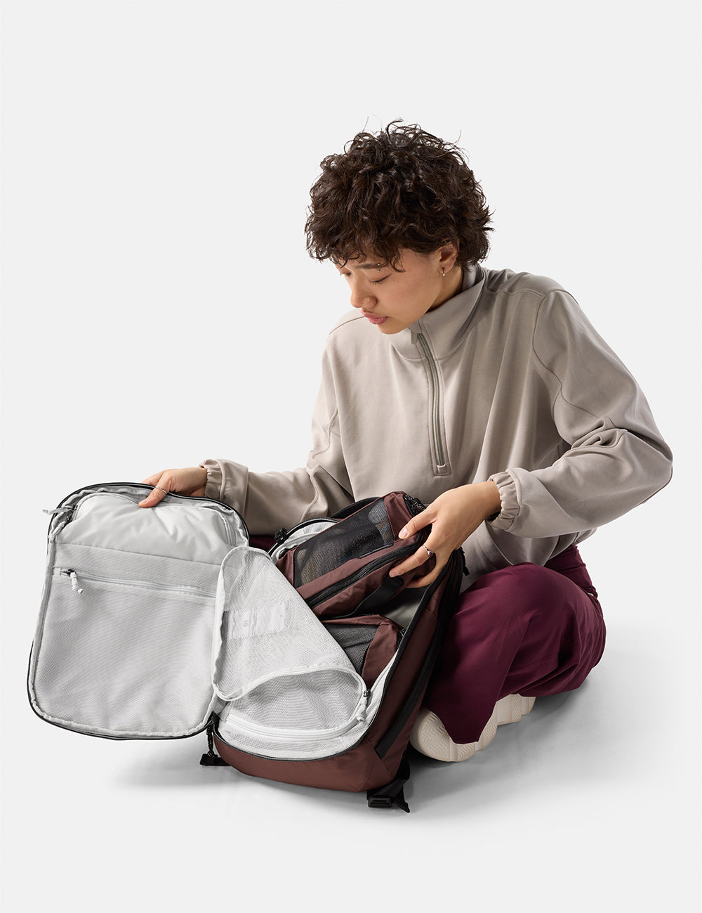 Person organizing a garnet backpack on a white background