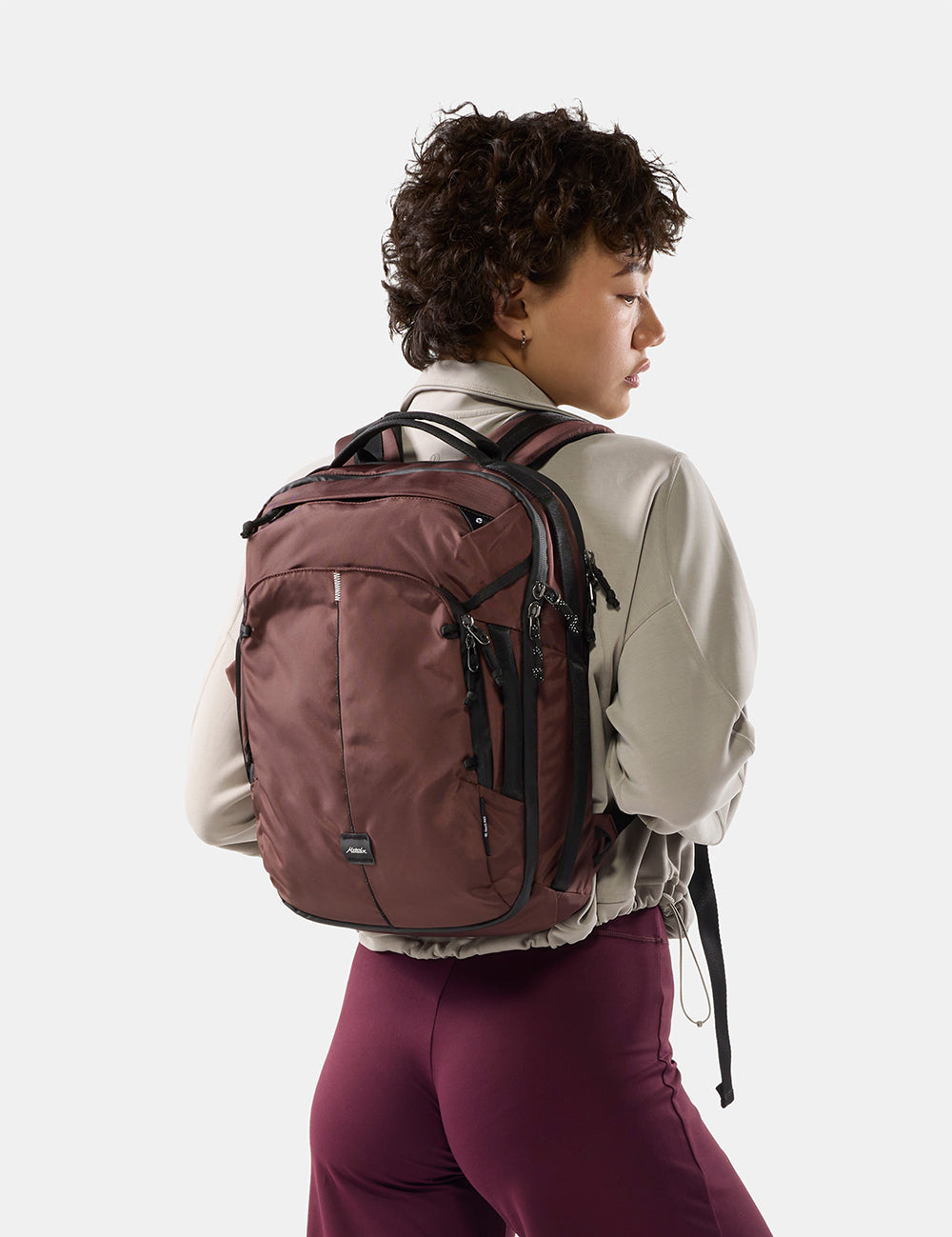 person on light gray background wearing a small garnet backpack
