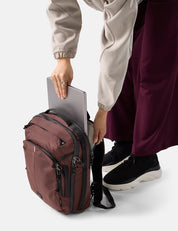 Person holding a laptop in a maroon backpack on a white background
