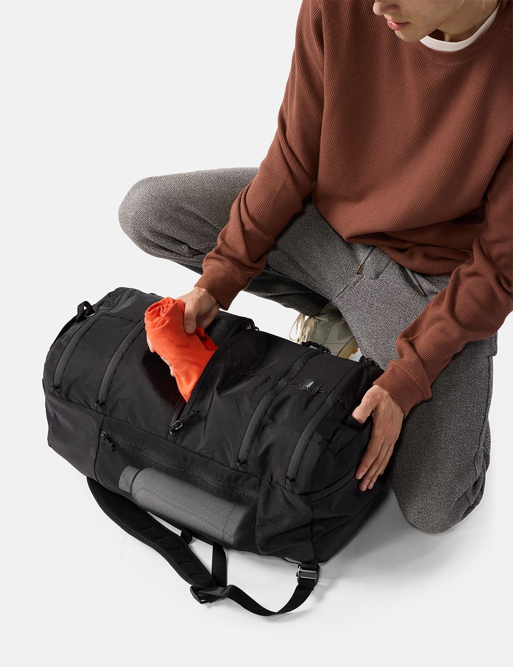 Person packing a black duffel bag with an orange item on a light gray background