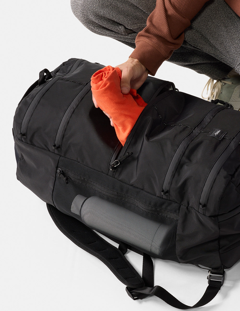 pulling orange jacket out of black segmented backpack