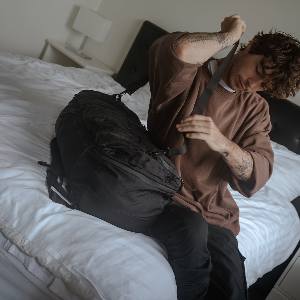 person on hotel bed, putting duffel over shoulder