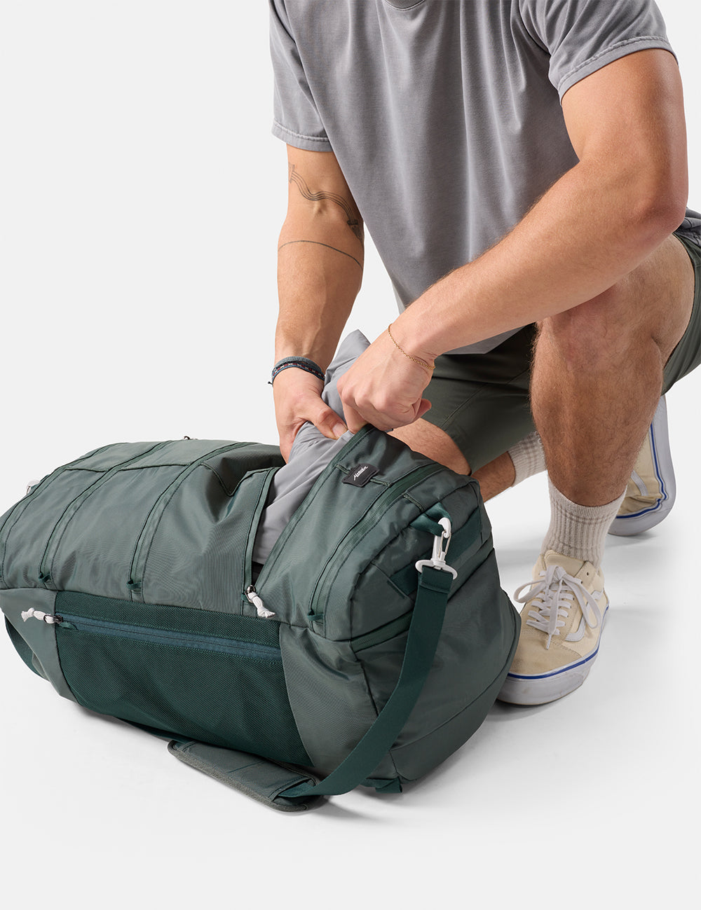 Person packing a green duffel bag on a white background