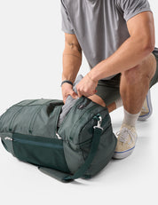 Person packing a green duffel bag on a white background