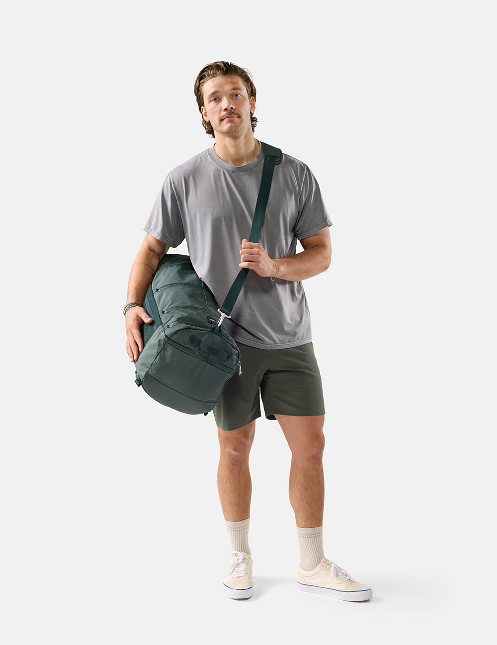 Man holding a green duffel bag against a white background