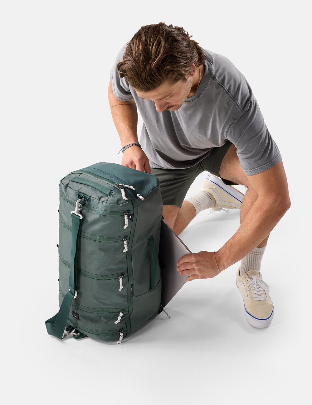Man unpacking a green backpack on a white background