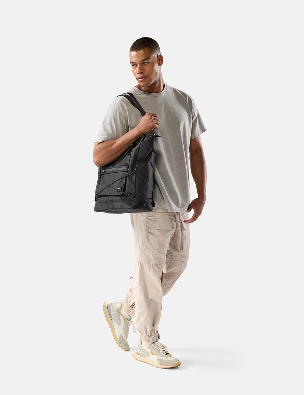 Man holding a black tote pack against a white background