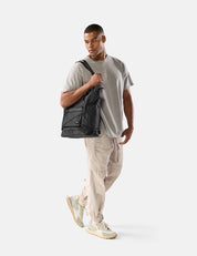 Man holding a black tote pack against a white background
