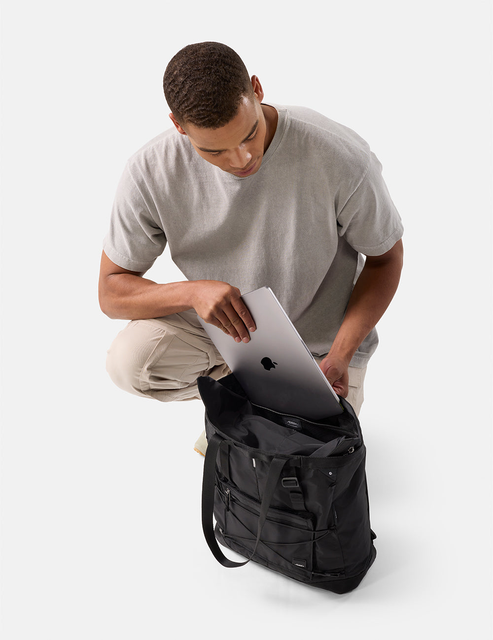 Man placing a laptop into a black tote pack on a white background
