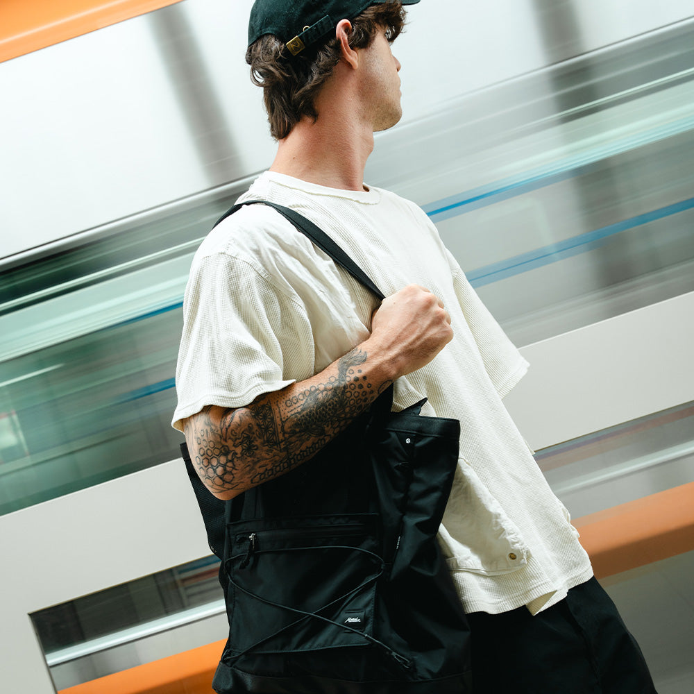 man in front of fast moving train with black tote