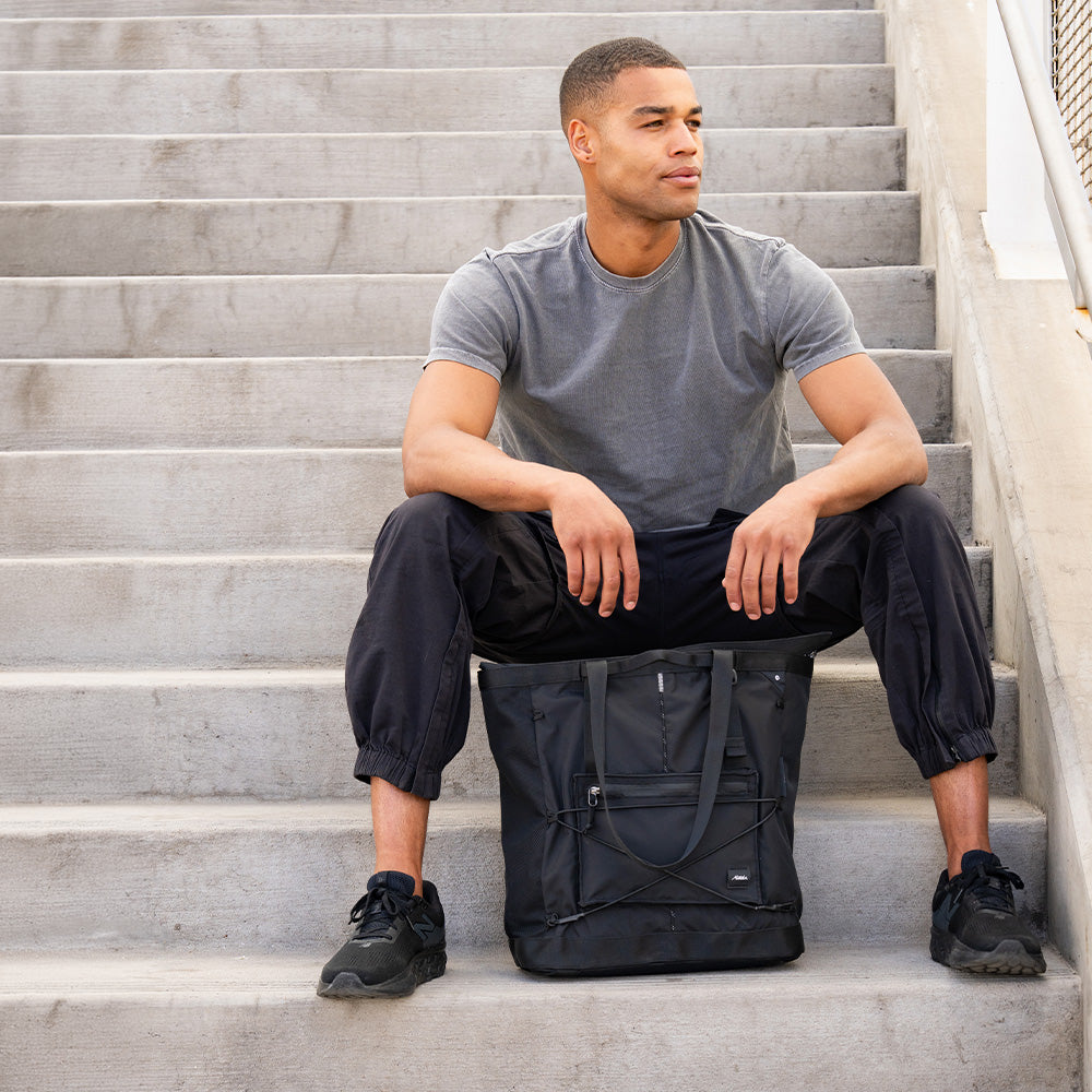 person sitting on concrete stairs with black tote