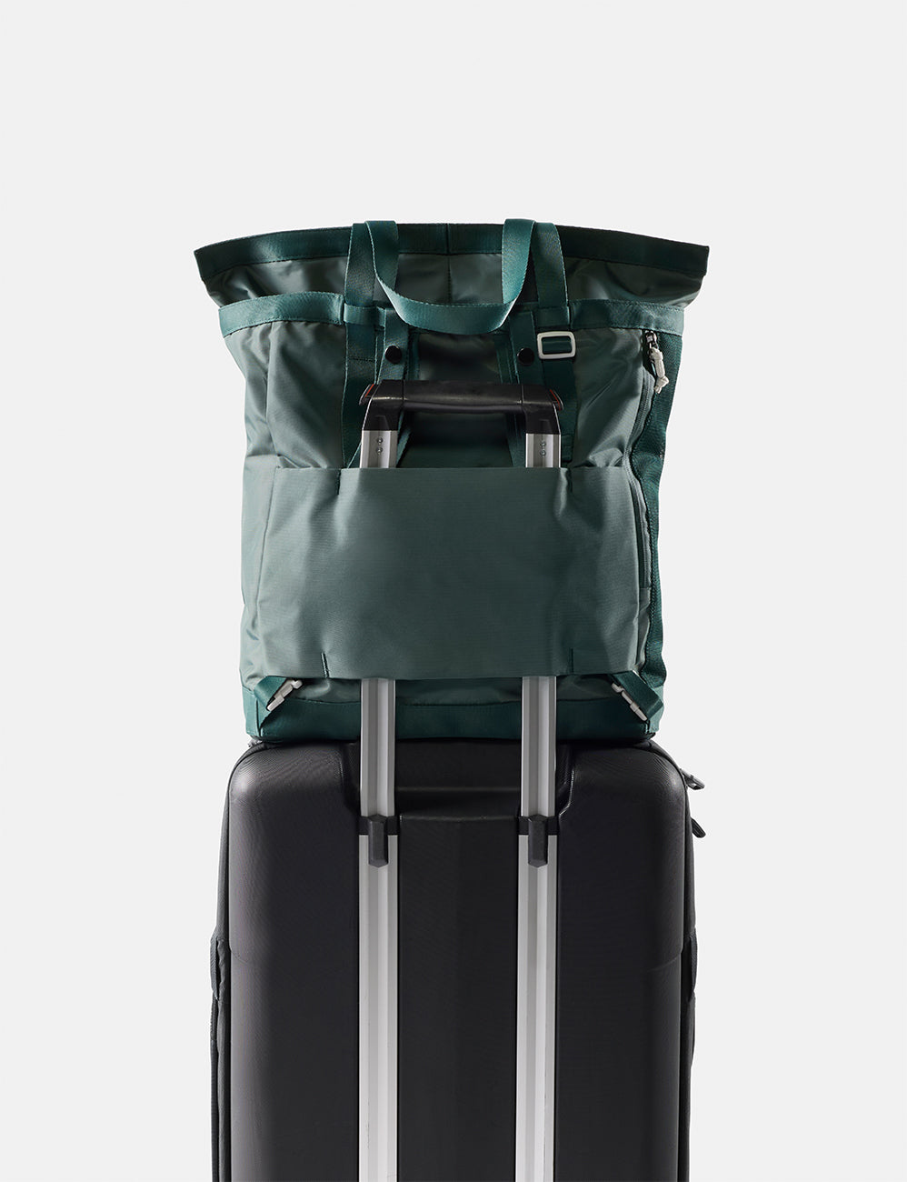 Green tote pack on top of a black suitcase with a white background
