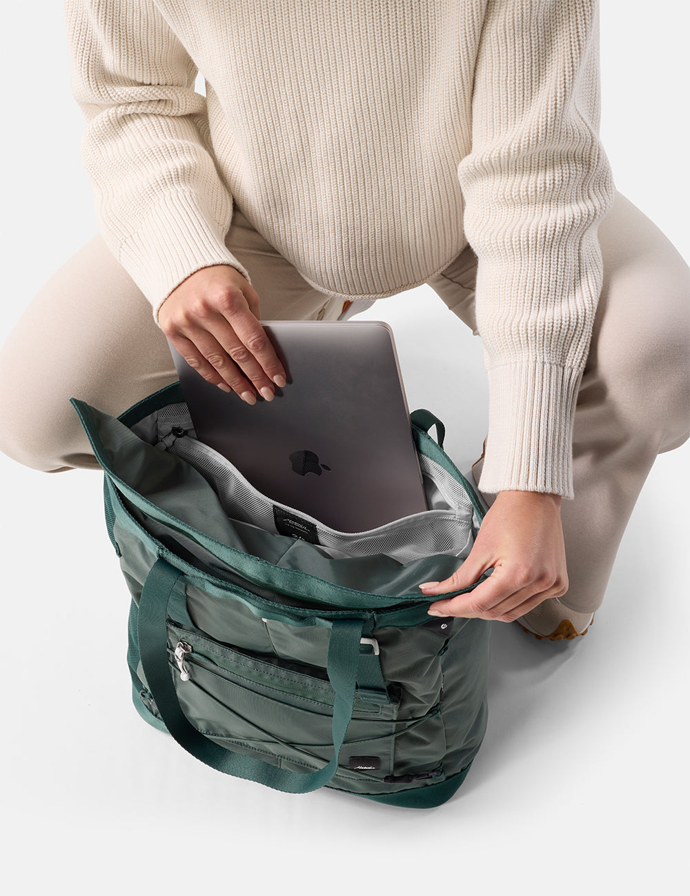 Person sitting with laptop and a green tote pack on a white background