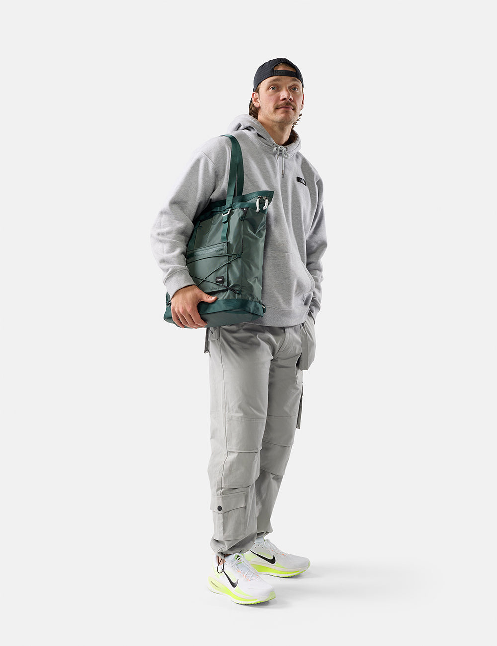 Person wearing a gray outfit with a green tote pack on a white background