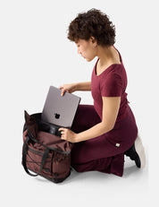 Woman in a burgundy dress placing a laptop into a garnet backpack on a white background