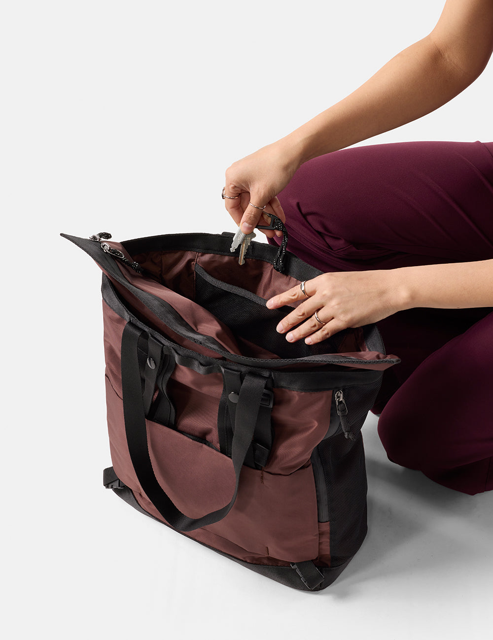 Person opening a maroon and black bag on a white background