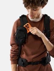 Person wearing a brown sweater pulling orange phone out of black speed stash