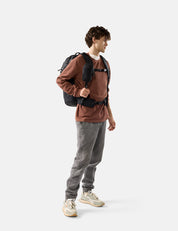 Person wearing a brown sweater, gray pants, and carrying a backpack on a white background
